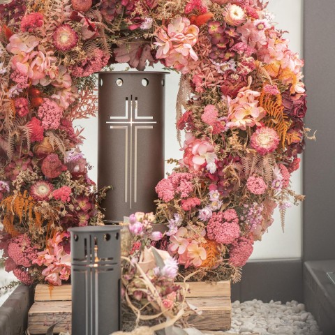 Grab mit einer bronzefarbenen Grablaterne mit Kreuzöffnung und einem großen Kranz aus getrockneten Blumen.